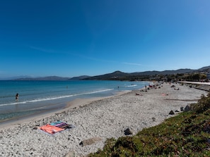 A beach with clear blue water, people sunbathing, and a colorful towel on the sand. - Chez Béatrice et Pascal by Interhome (Lozari)