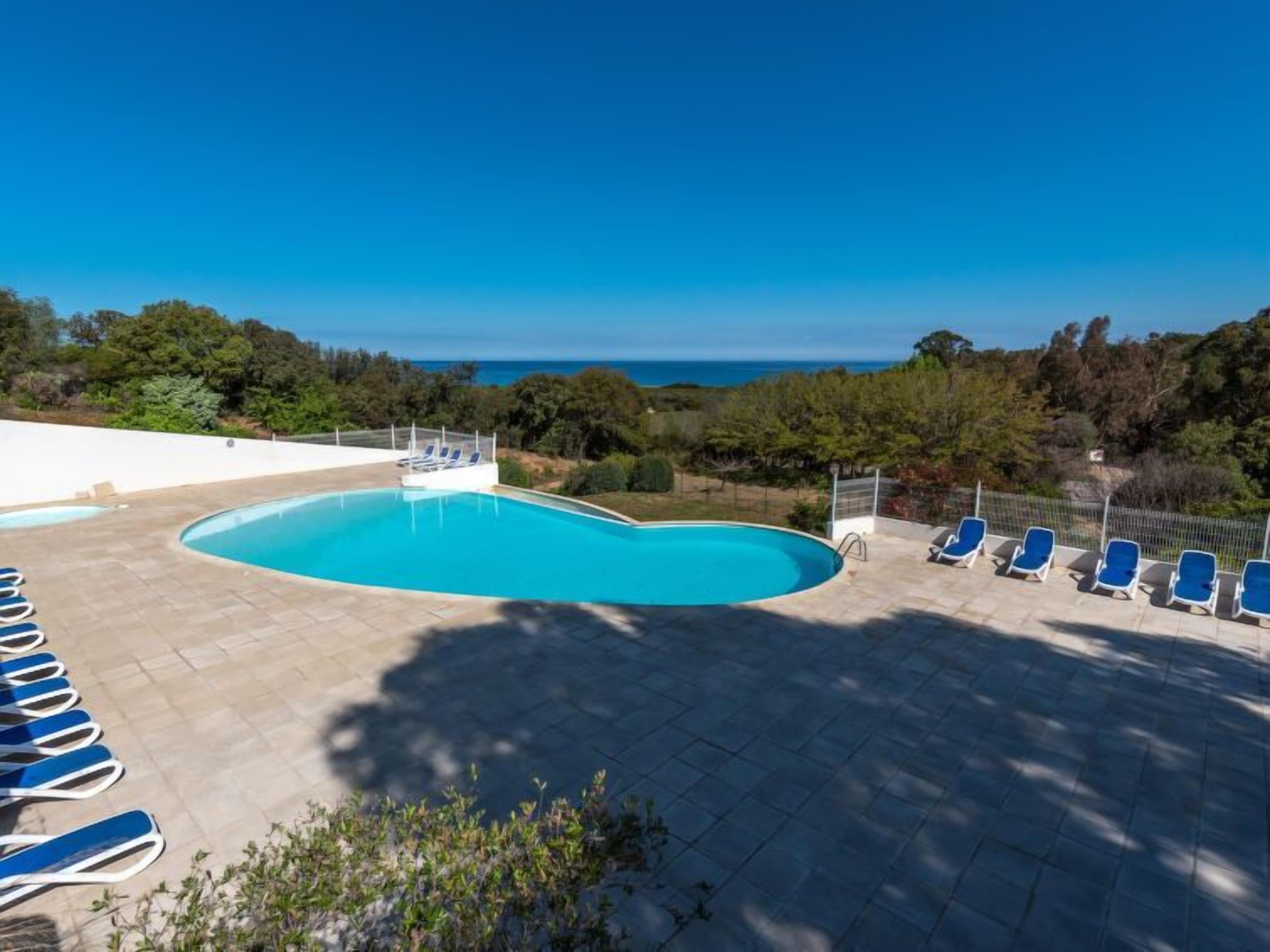 Una piscina con sillas de descanso, rodeada por una terraza de baldosas y vistas al mar.