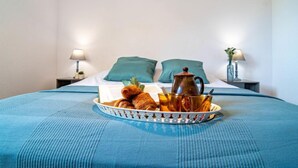 A neatly made bed with a blue bedspread, two pillows, a tray with croissants and a coffee pot, and two bedside lamps. - Le Panama by Interhome (Saint Aygulf)