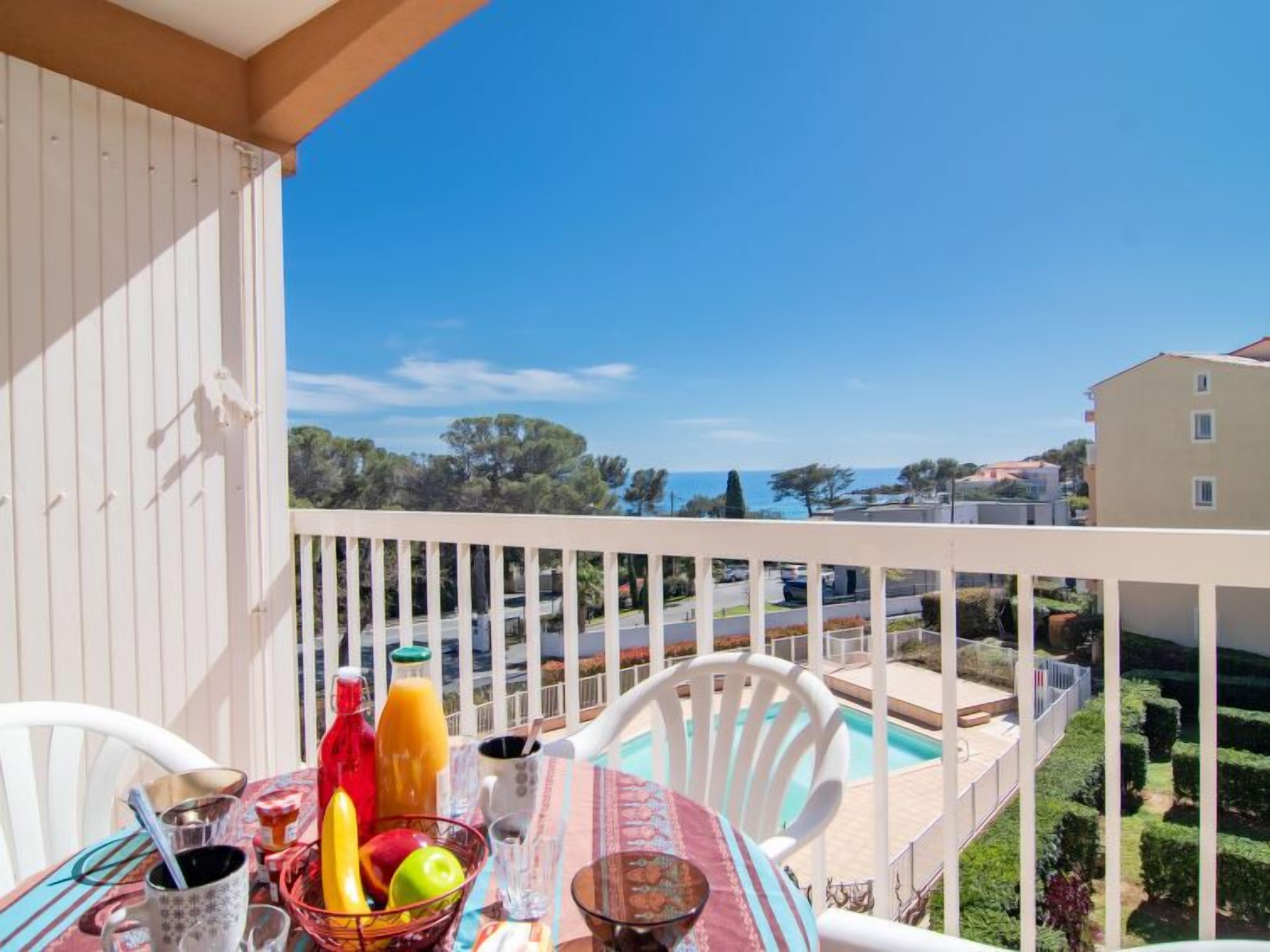 Ein Balkon mit Frühstückstisch, einem Pool und Blick auf das Meer und Gebäude.