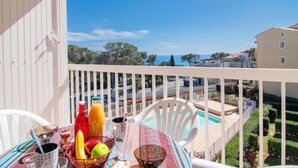 A balcony with a table set for breakfast, a pool, and a view of the sea and buildings. - Le Panama by Interhome (Saint Aygulf)