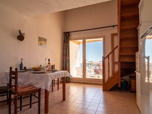 Zona pranzo con tavolo apparecchiato per due, una sedia di legno e vista all'esterno tramite una porta in vetro.