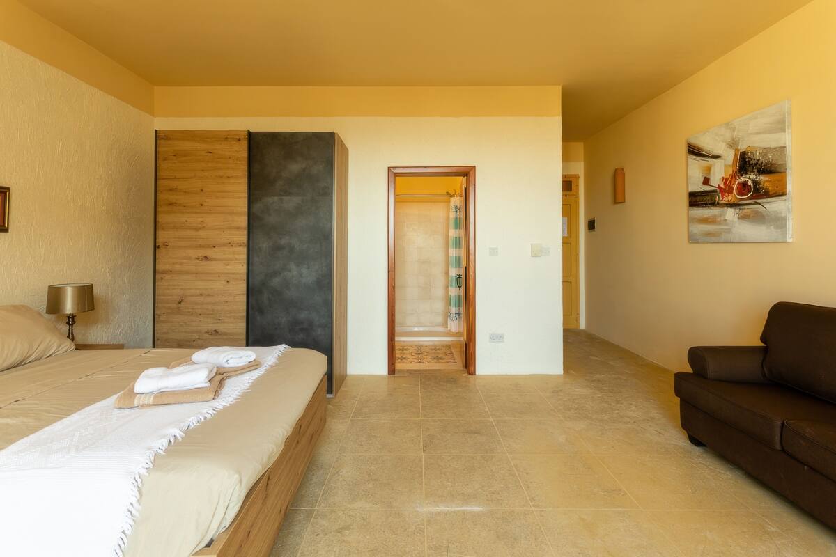 A hotel room with a large bed, a wooden accent wall, a brown sofa, and a painting on the wall.