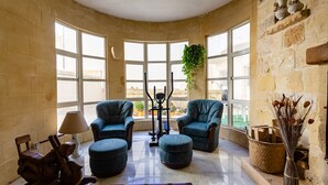 A room with large windows, two blue armchairs, a wooden rocking horse, a lamp, and a plant. - Villa Serenity B&b (Sannat)