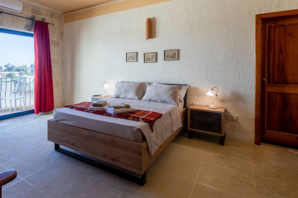 A bedroom with a wooden bed, two bedside tables with lamps, a red curtain, and a wooden door.