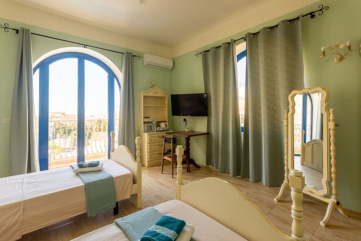 A room with a bed, a desk, a chair, a TV, and a large window with curtains.