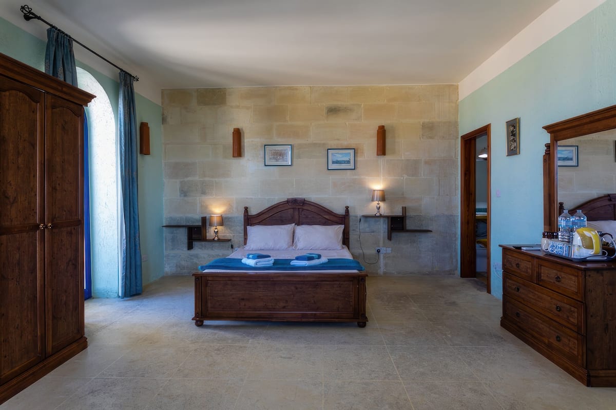 A bedroom with a wooden bed, stone walls, a wardrobe, and a dresser.