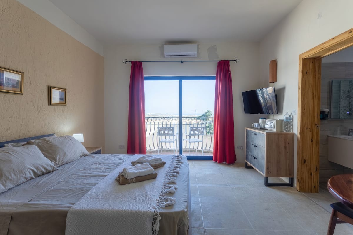 A bedroom with a bed, a TV, a desk, and a balcony with red curtains.