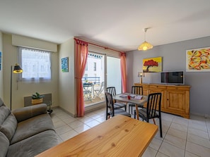 A compact living space with a sofa, dining table, chairs, a TV, and a sliding glass door leading to an outdoor area.