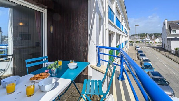 Een balkon met een ontbijttafel, uitzicht op de straat en een blauwe balustrade.