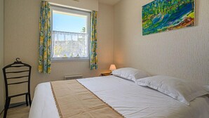 Een slaapkamer met een bed, een raam met gordijnen, een schilderij aan de muur en een stoel.