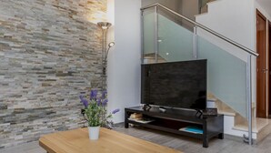 Una sala de estar moderna con una pared de piedra, un banco de madera, un televisor sobre un mueble bajo y una escalera.