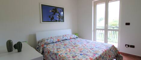 A bedroom with a bed, a dresser, a cactus, a painting, and a window.