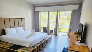 Habitación de hotel con una cama grande, un banco de madera, un escritorio con televisor y vistas a un jardín por la ventana.