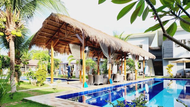 Zona de piscina con una estructura de techo de paja, sillas de descanso y una piscina azul cristalina.