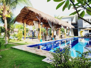 A pool area with a thatched-roof structure, lounge chairs, and a clear blue pool. - Danbi Resort (Panglao)