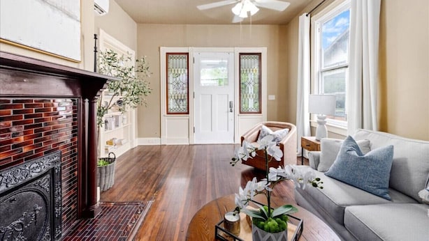 A spacious living room with hardwood flooring, a fireplace, a ceiling fan, and a sofa with cushions. - Downtown Heritage Suite | Free Parking (Macon)