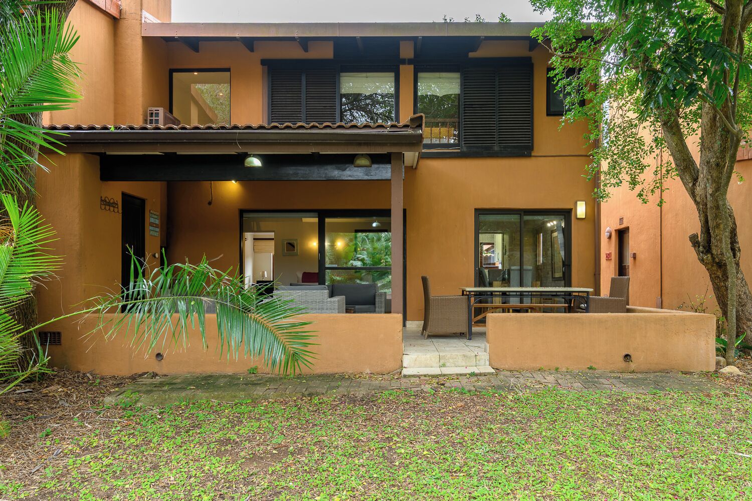 A two-story building with a covered patio area, a seating arrangement, and a tree in the foreground.