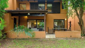 A two-story building with a covered patio area, a seating arrangement, and a tree in the foreground.