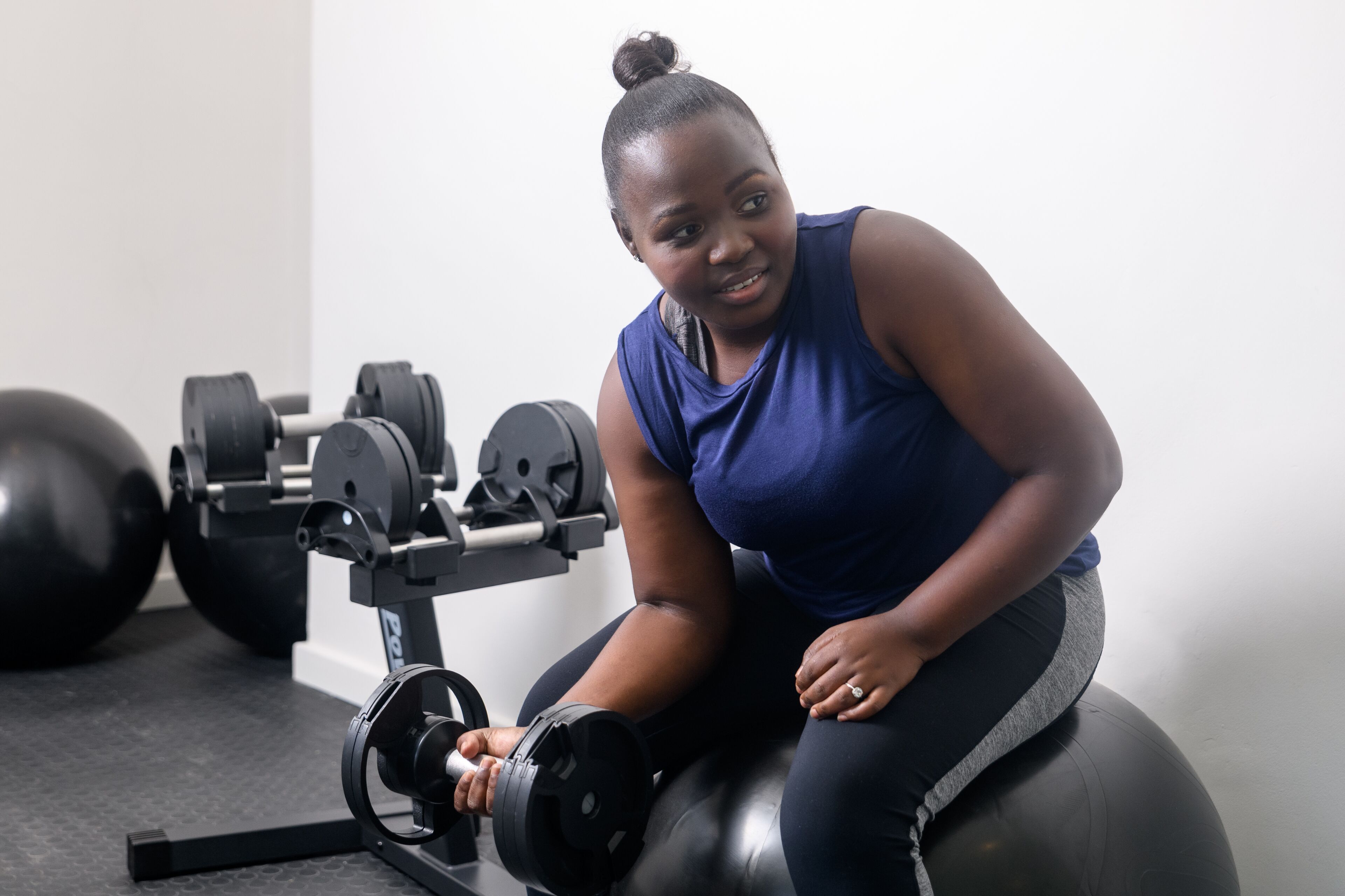 Uma pessoa usando uma máquina de cadeira para exercícios de pernas em uma academia, com pesos e uma estrutura de barra para agachamento ao fundo.