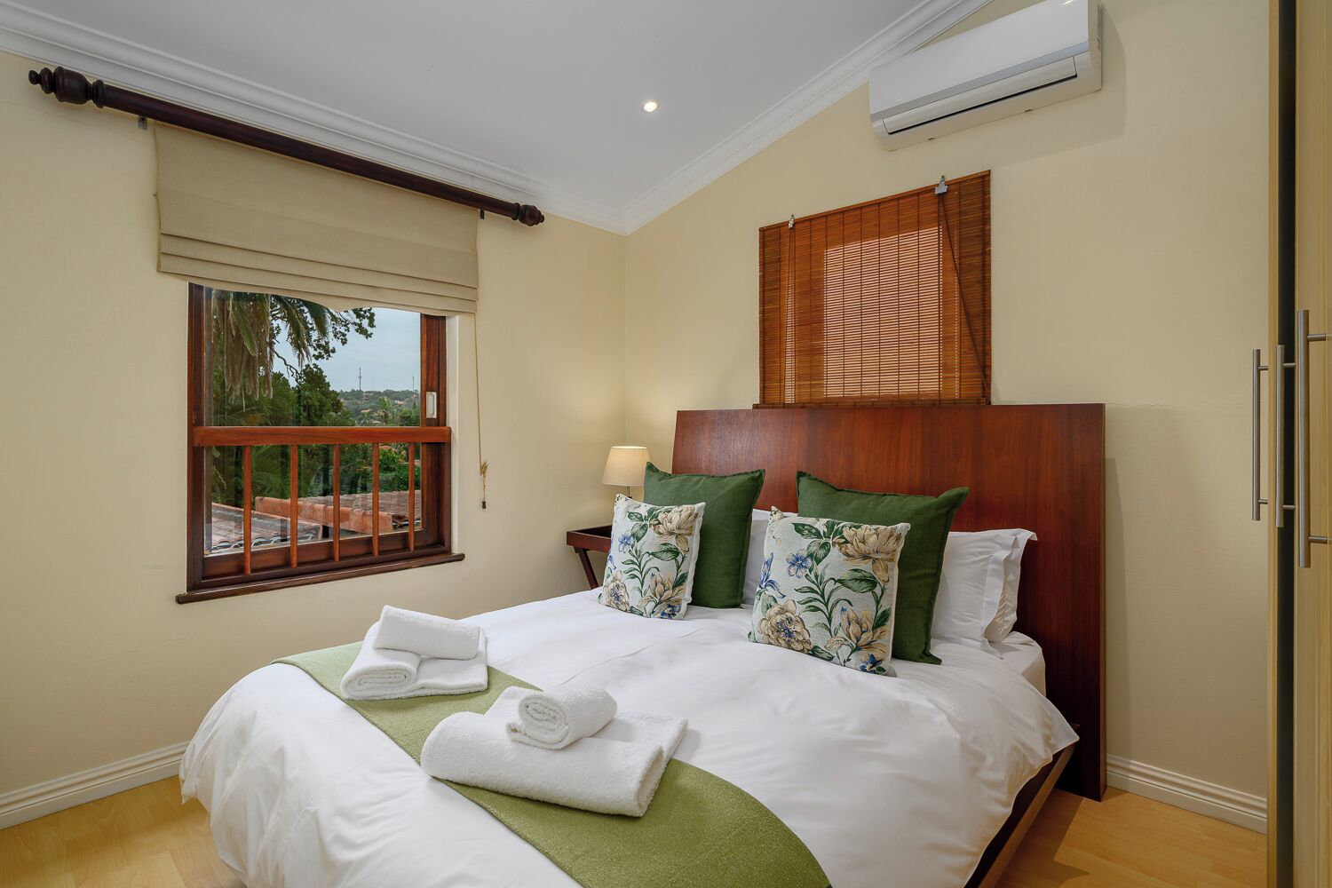 A hotel room with a large bed, a window with a view, an air conditioning unit, and a wooden headboard.