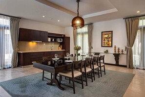 A modern dining room with a large table set for six, a kitchen area with dark cabinetry, and a decorative pendant light.
