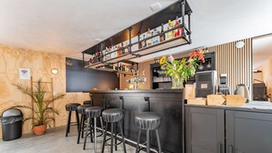 A bar area with stools, a shelf of bottles, a potted plant, and a coffee machine.