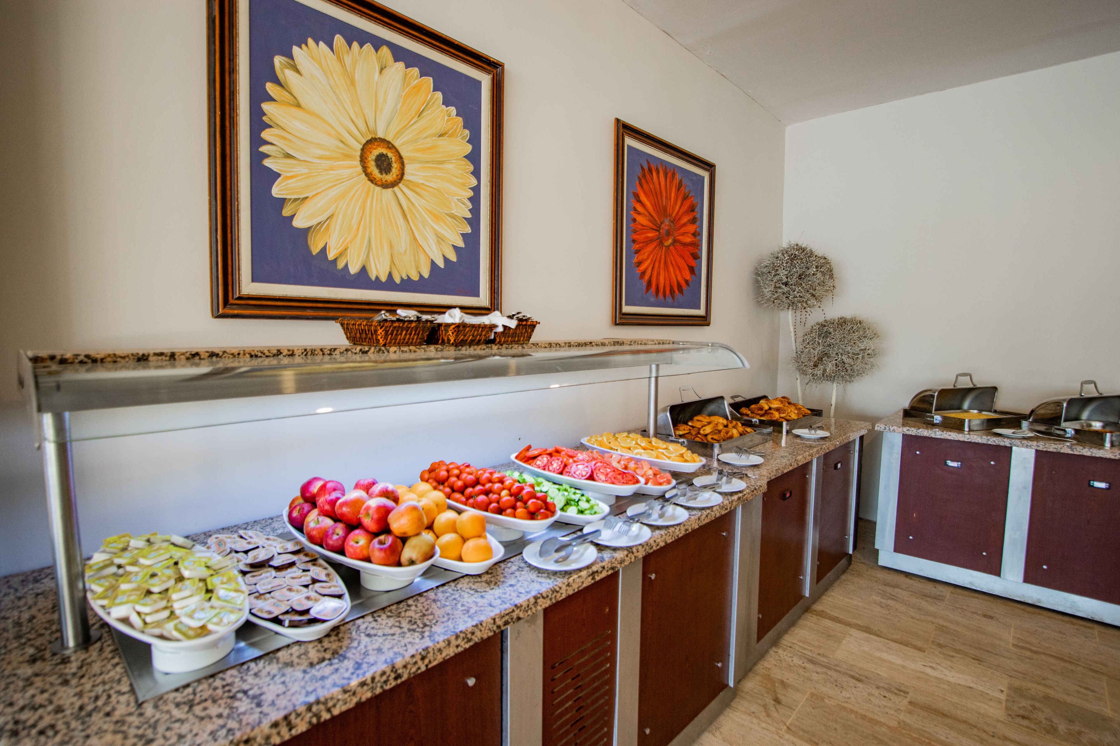 Un buffet proposant une variété de fruits et de légumes, un mur décoratif orné de peintures florales et une petite plante en pot.