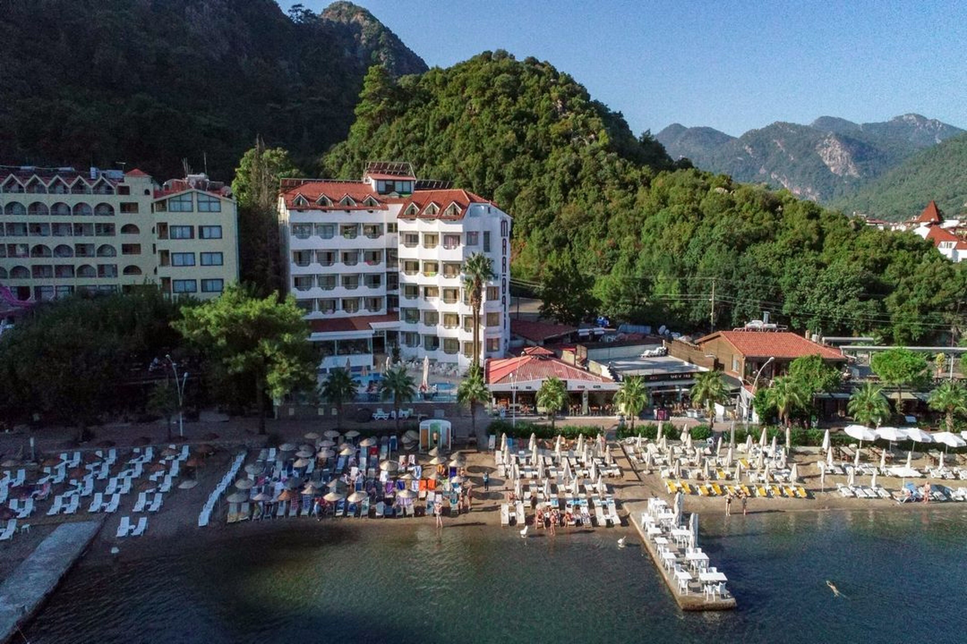 Um hotel à beira-mar com vários andares, área de praia com espreguiçadeiras e um cais.