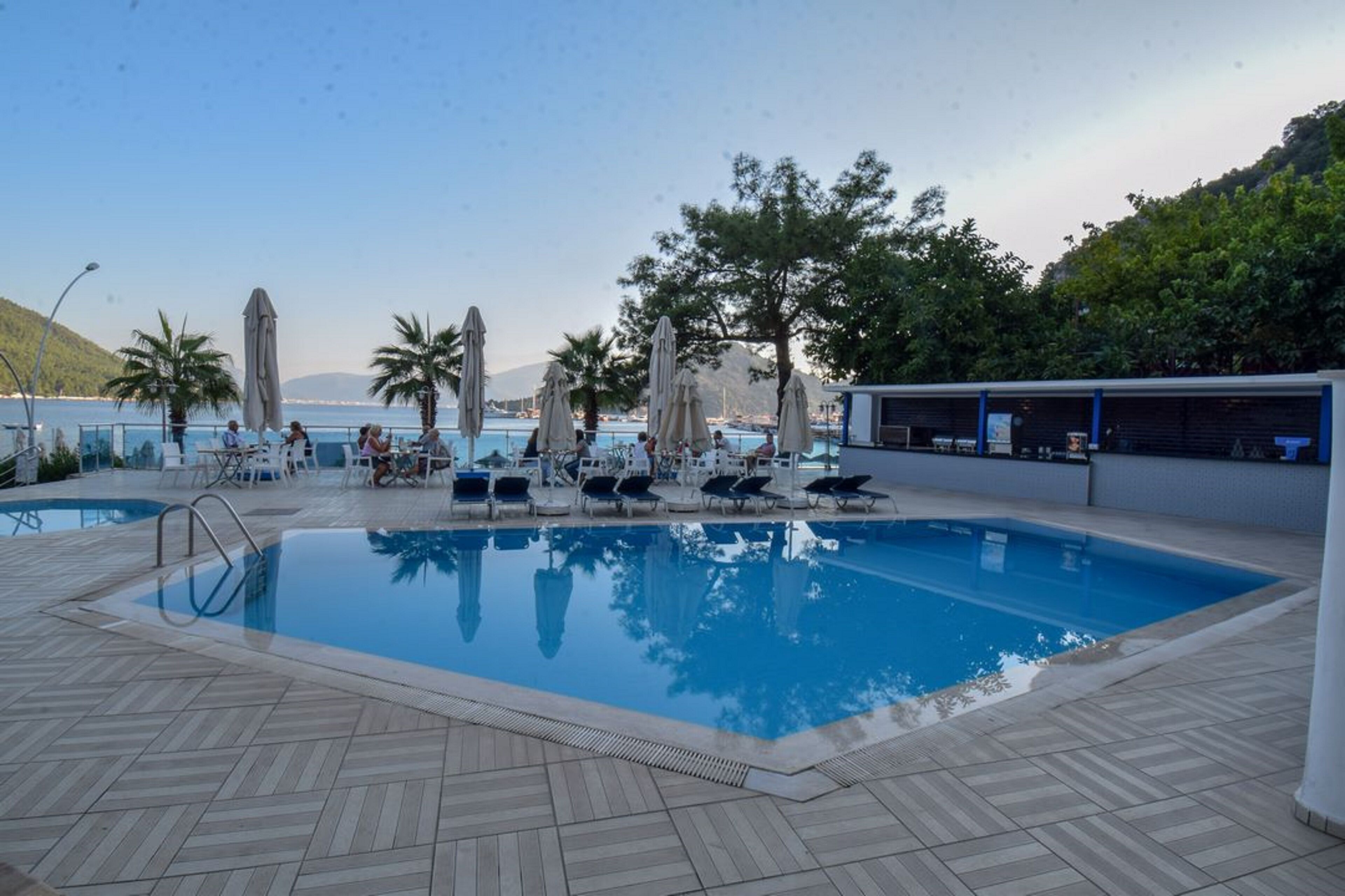 A swimming pool with lounge chairs and umbrellas, surrounded by trees and a view of the sea.