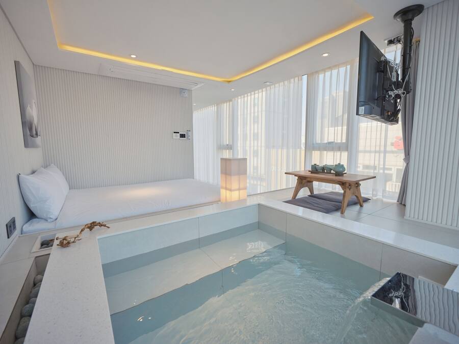 A modern bathroom with a glass-enclosed hot tub, a wooden bench, and a large mirror.