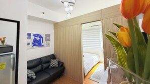 Una habitación de hotel moderna con un sofá de cuero negro, una cama con edredón blanco, un armario de madera y un jarrón de vidrio con tulipanes.
