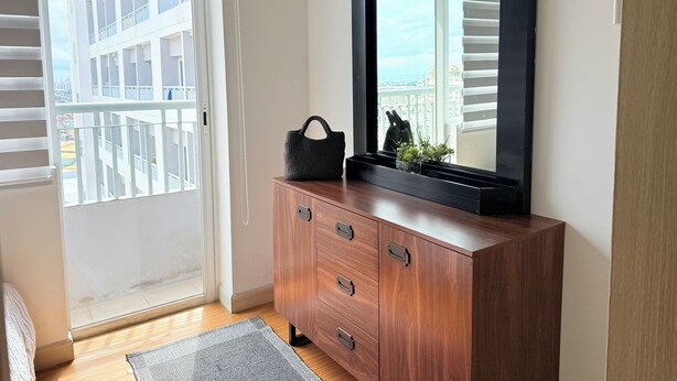 Una habitación con un armario de madera, un espejo y vistas a un edificio a través de una ventana con persianas.