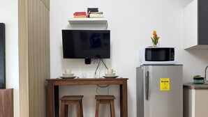 Una kitchenette compacta con microondas, refrigerador y televisor de pantalla plana montado en la pared.