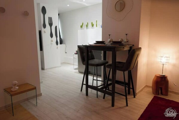 A dining area with a table and two chairs, a small table with a sculpture, and a wall with utensils and plants.