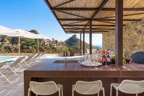 An outdoor bar area with a stone wall backdrop, a pool, and lounge chairs.