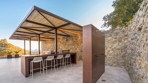 Een terras met een bar, een stenen achtergrondmuur, een metalen dak en barstoelen.