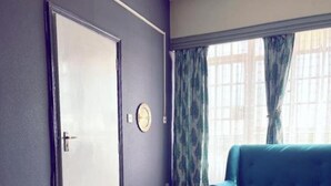 A hotel room with a bed, a blue sofa, a door, and a window with curtains. - Miami Global Hotel (Nairobi)