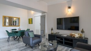 Un salon moderne avec une table basse en verre, des canapés gris, un coin repas avec des chaises vertes, un téléviseur à écran plat et des objets décoratifs sur la console.