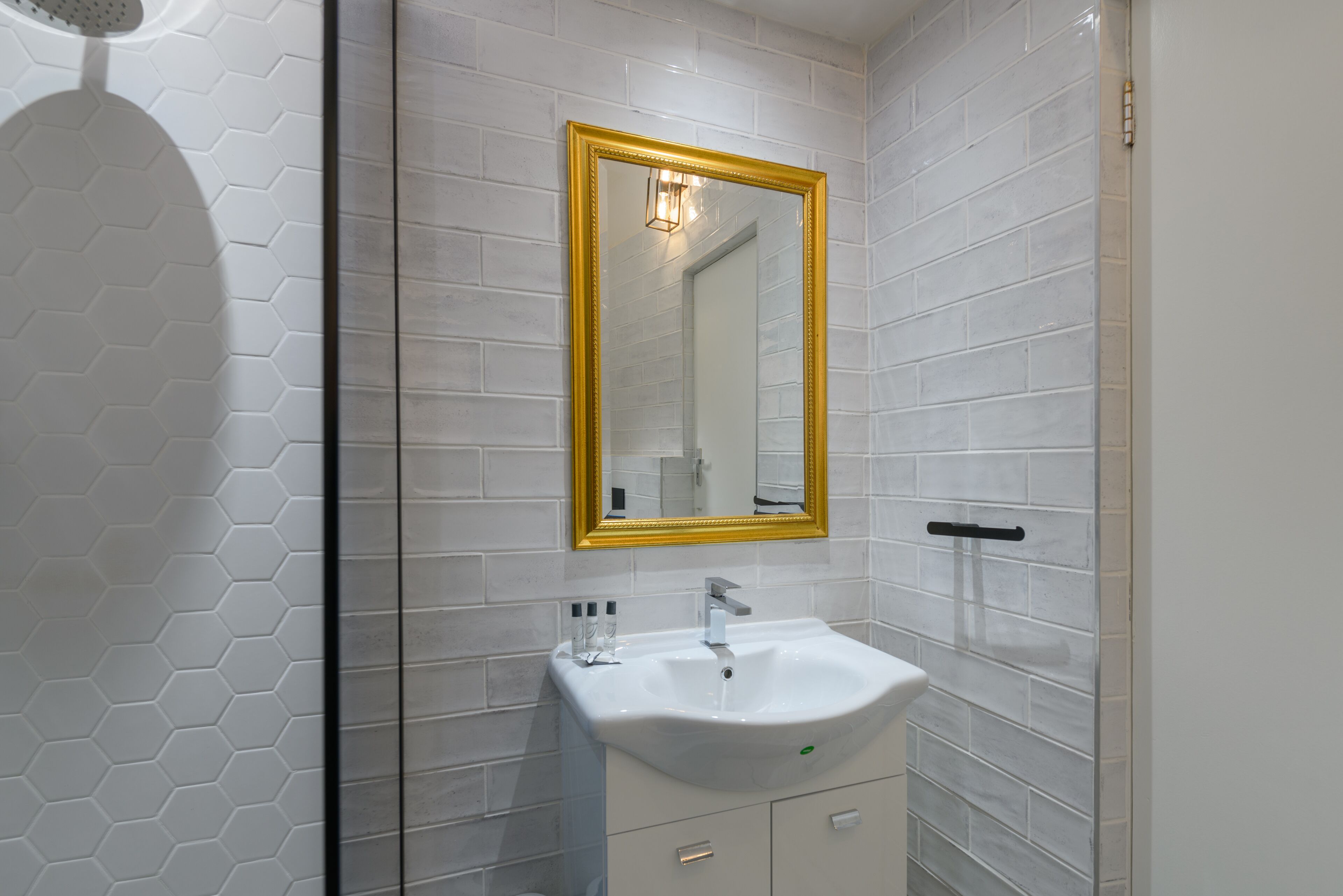 A bathroom with a white sink, a gold-framed mirror, and a shower with a hexagonal tile pattern.