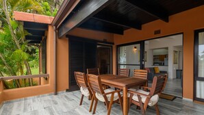 Un espace repas avec une table et des chaises en bois, un patio couvert et une vue sur la cuisine et le salon.