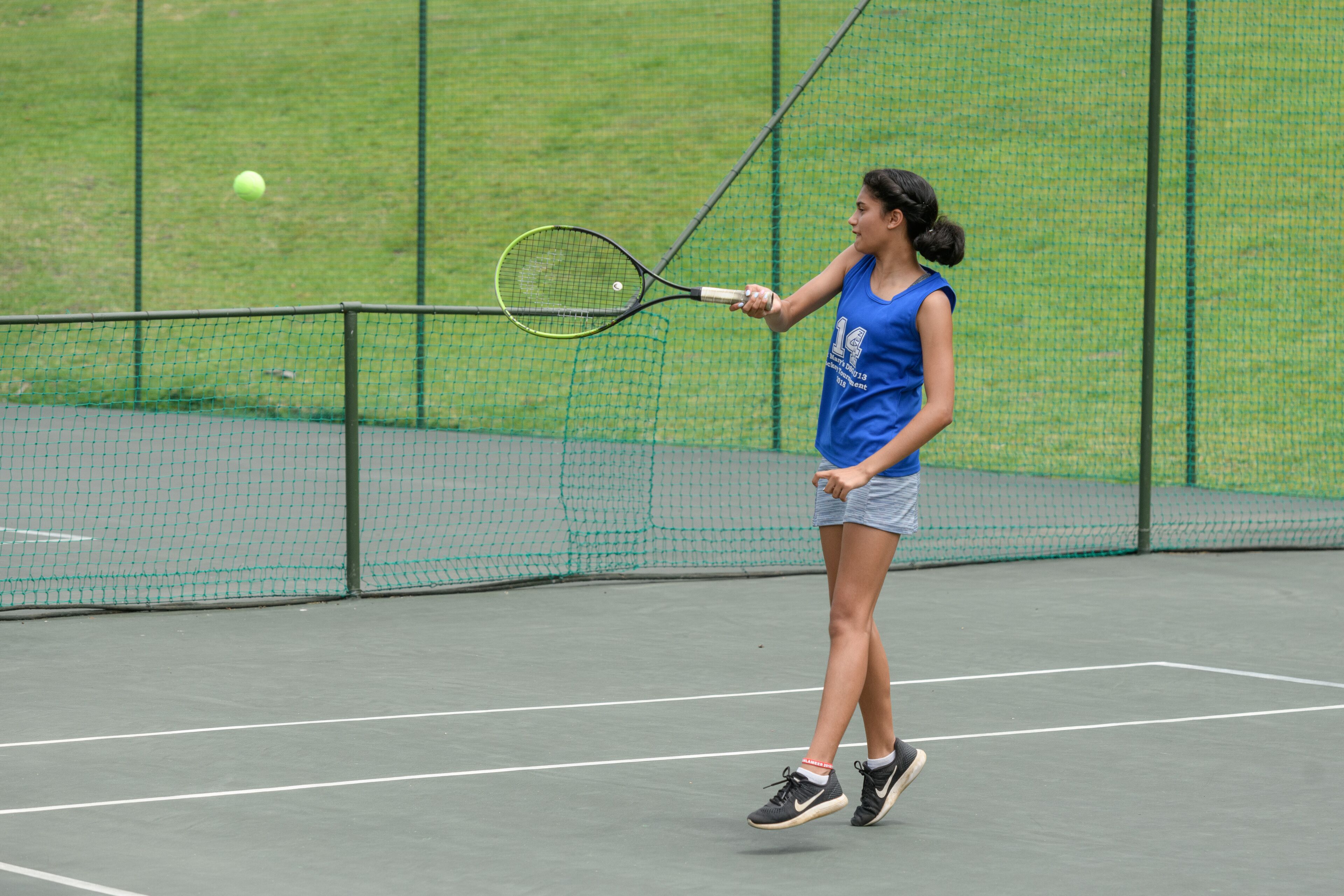 Una cancha de tenis con red, un jugador con camisa y pantaloneta azules, y una pelota de tenis en movimiento.