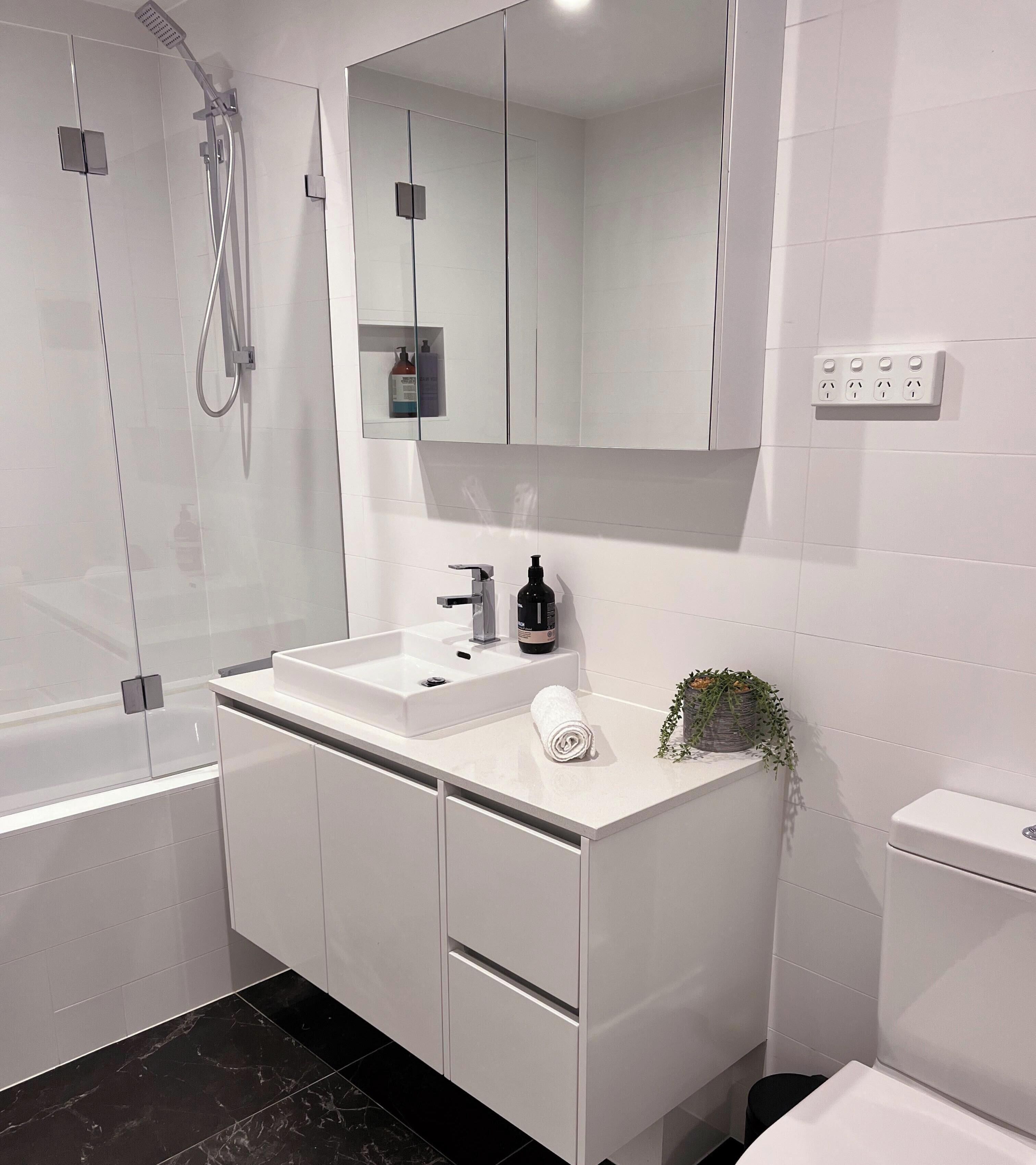 A modern bathroom with a glass-enclosed shower, a white sink with a mirror above, and a toilet.