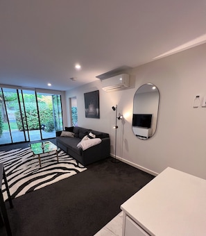 Een moderne woonkamer met een bank, een glazen salontafel, een tapijt met zebraprint, een grote spiegel en een televisie.