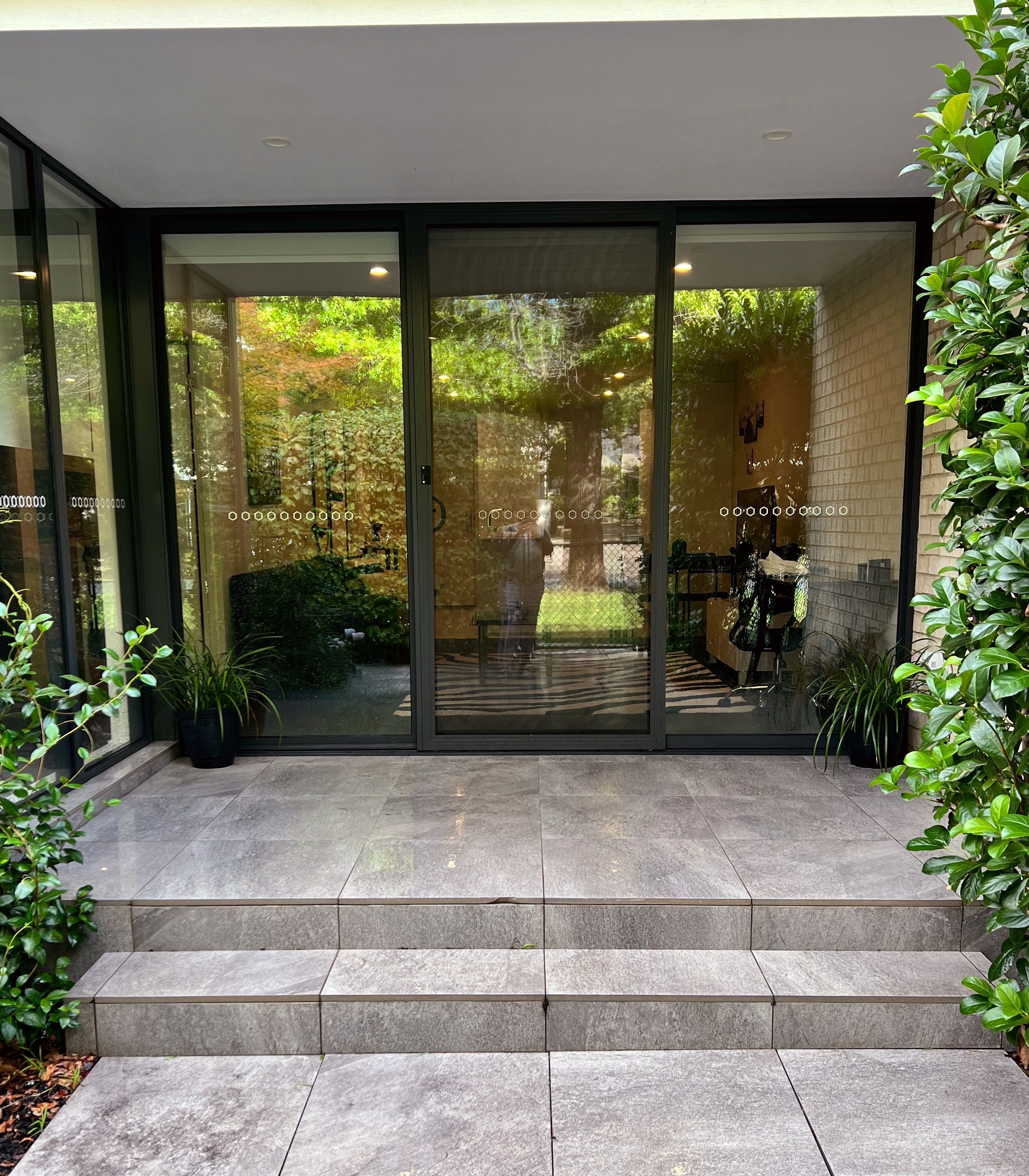 A modern building entrance with glass doors, a tiled patio, and potted plants.