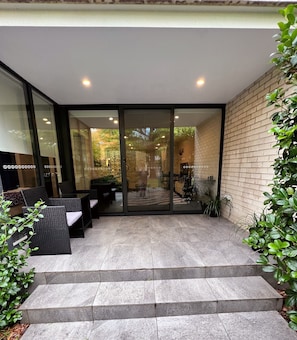 Een modern buitenterras met glazen deuren die leiden naar een zithoek, stenen trappen en potplanten.