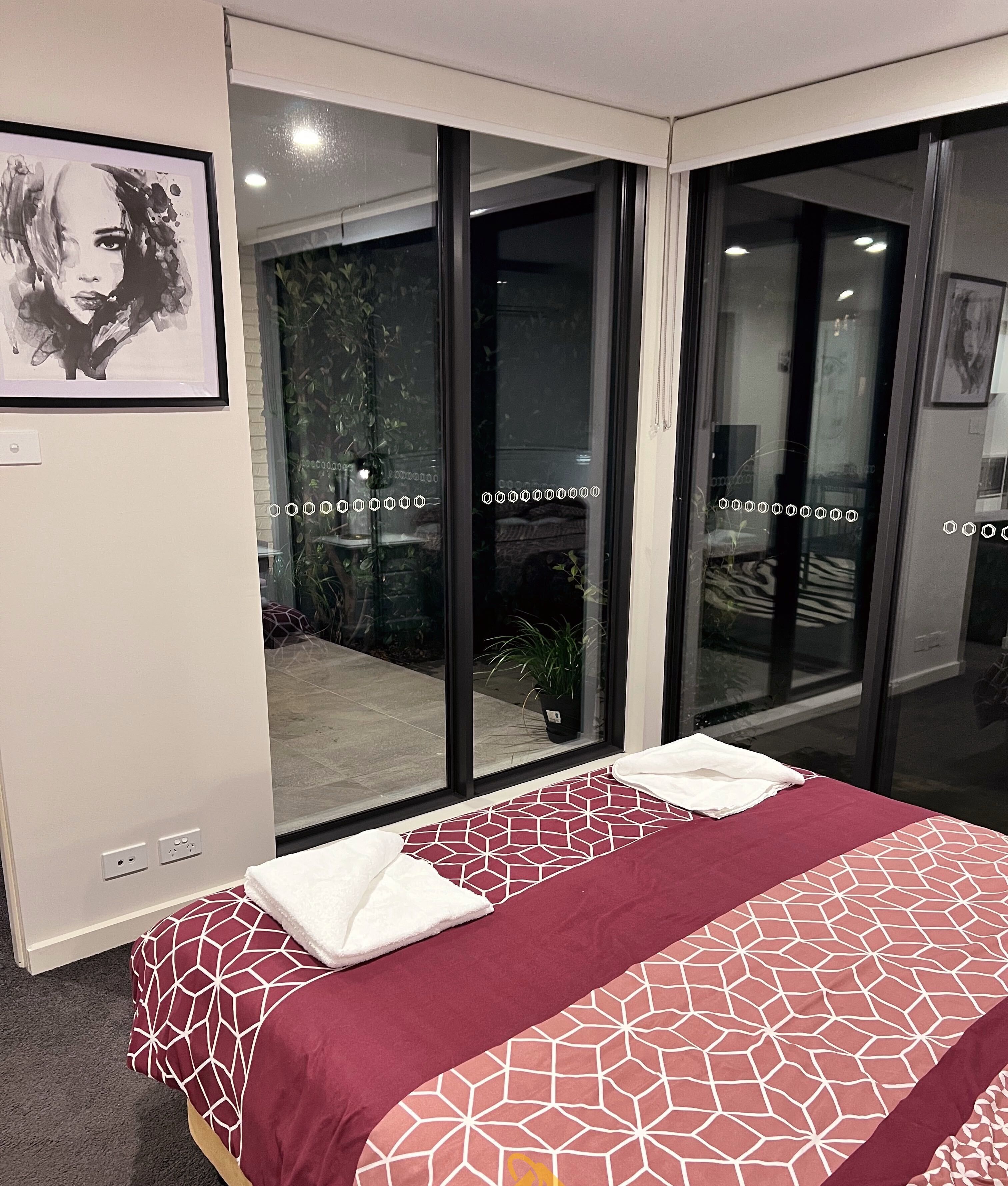 Une chambre d’hôtel avec un grand lit, une vue sur l’extérieur grâce à des portes vitrées donnant sur un espace extérieur, et une œuvre d’art encadrée au mur.