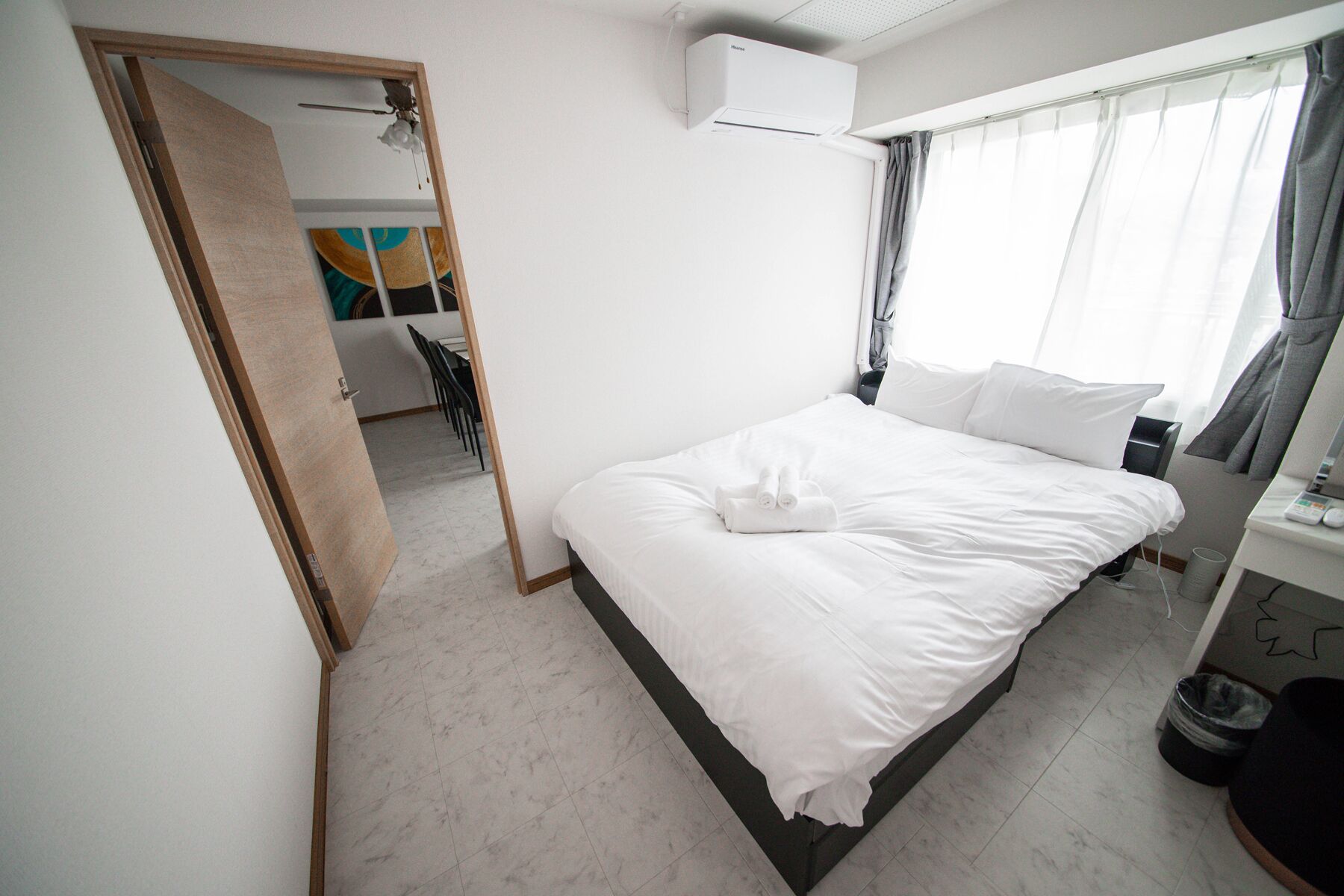 A clean, modern hotel room with a bed, a desk, and a window with curtains.