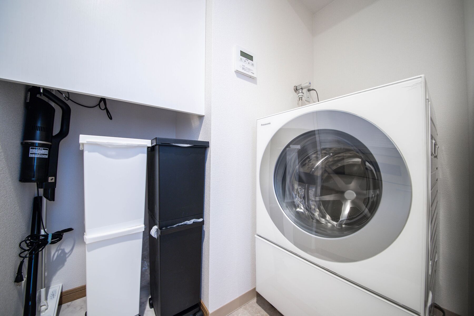 Un lavadero pequeño con lavadora de carga frontal, un refrigerador compacto y un aspirador.