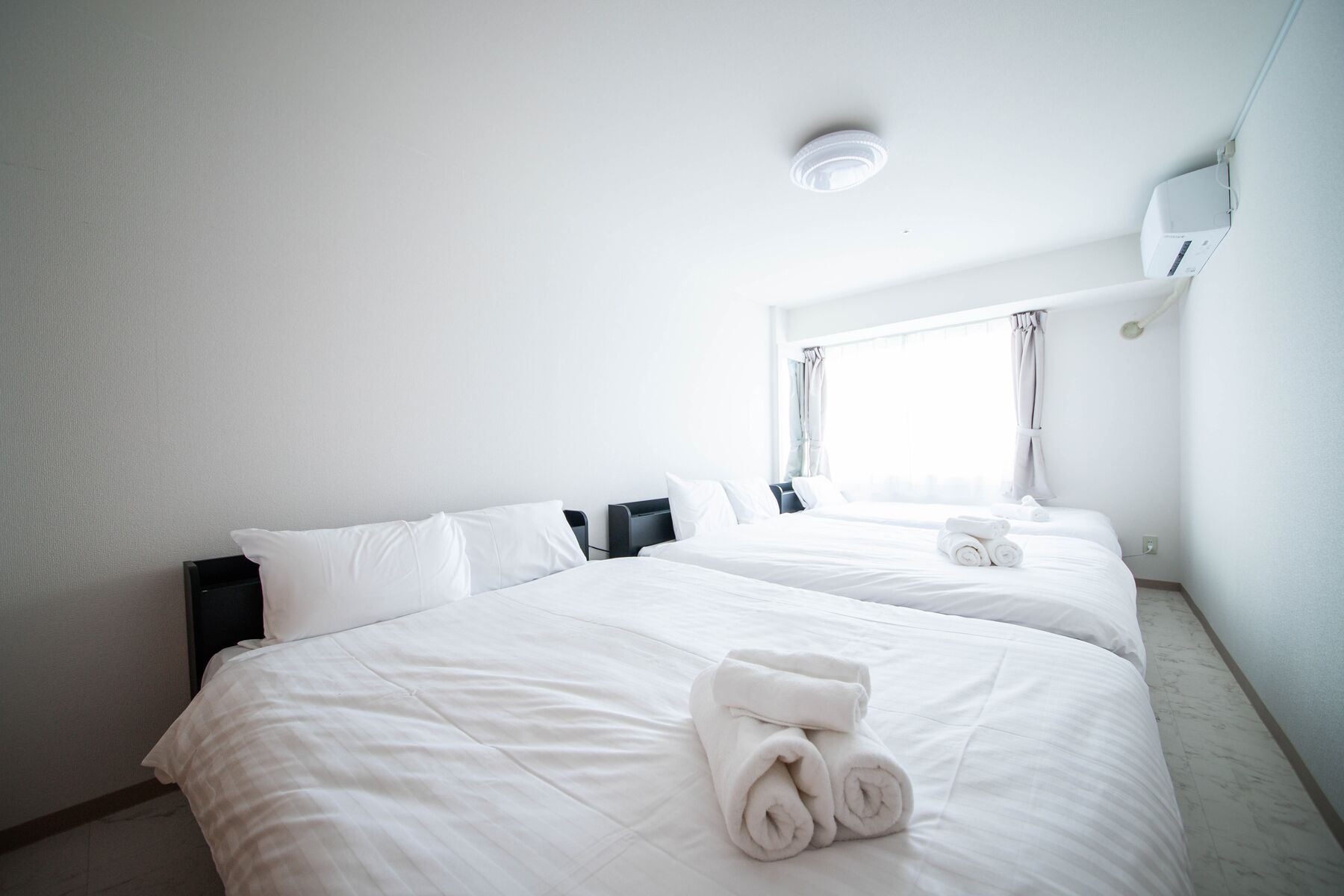 Ein Hotelzimmer mit einem großen Bett, einem Nachttisch, einem Fenster mit Vorhängen und einer Deckenleuchte.